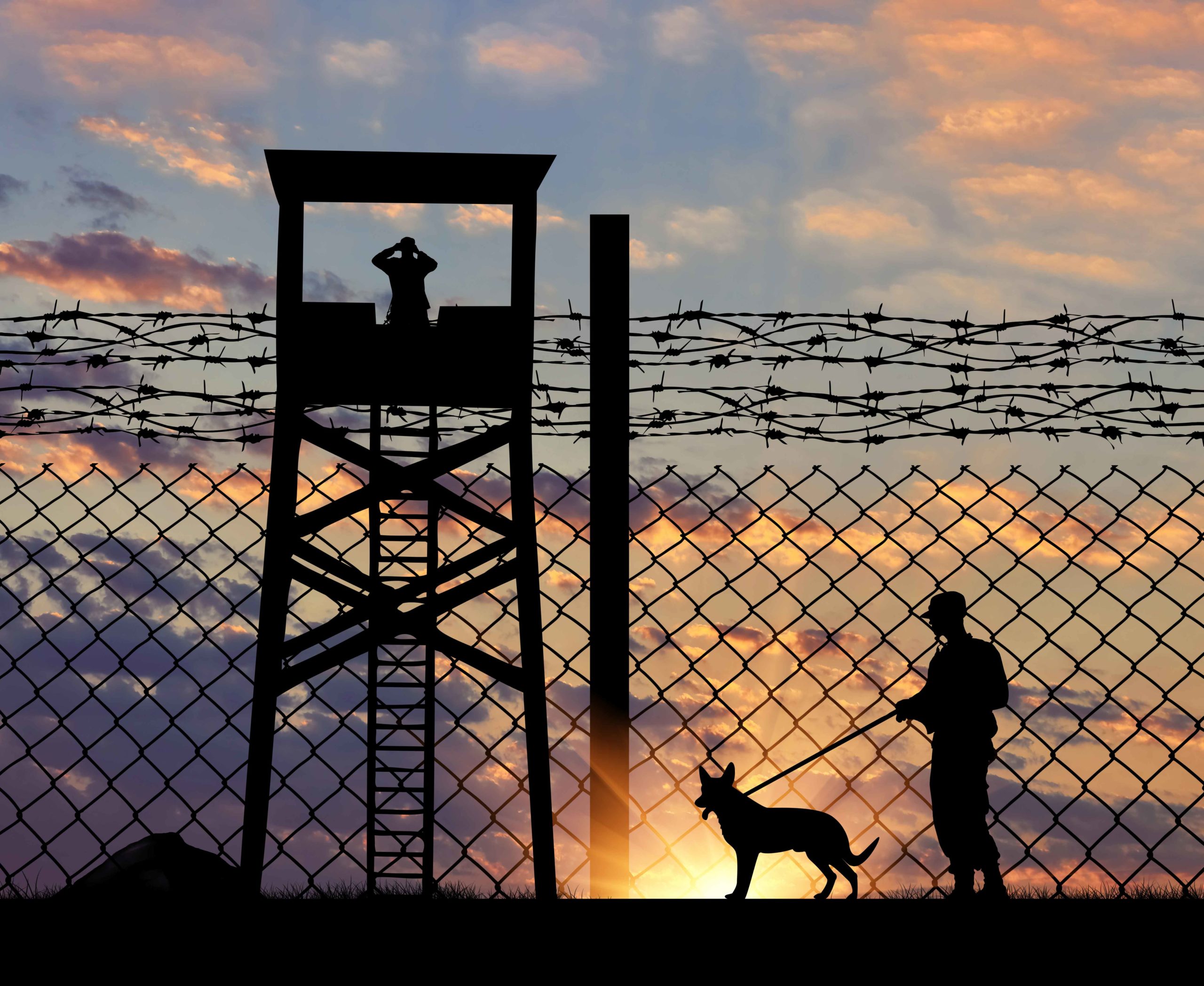 Guardias de seguridad a contraluz tras verja de cárcel y en torre de vigilancia